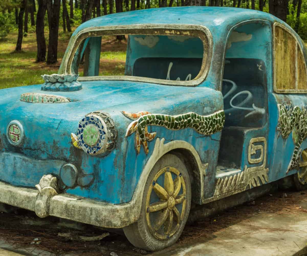 A mosaic filled, sky blue car sits still, 'rusting' away