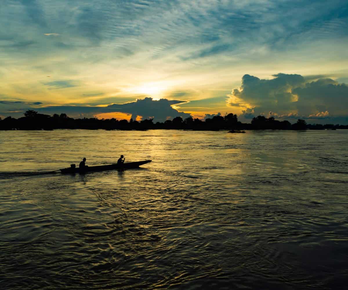 Don Det sunrise with locals cruising the Meekong River in a long-tail style boat