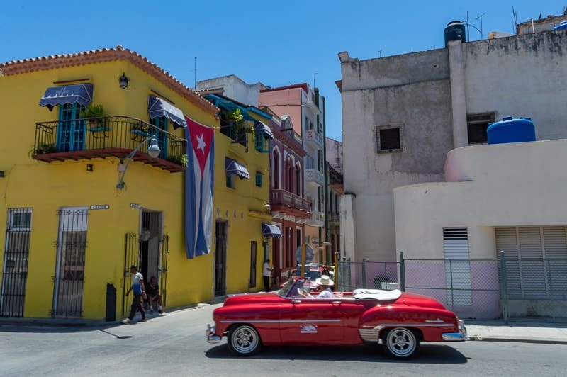 A vibrant red classico car next to the Cuban flag